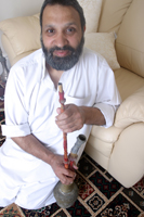 Colour photograph of Irshad Akbar sitting with his fathers Chillum/ pipe.