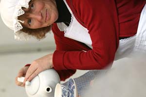 Colour photograph of the head and shoulders of Nikky Wilson in maids costume pouring tea