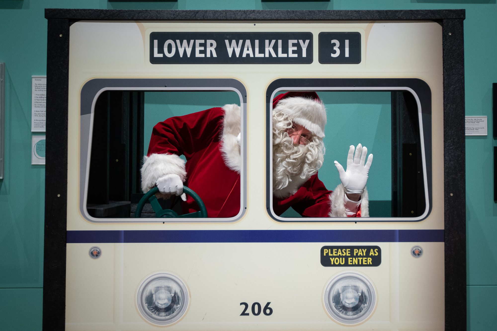 A photograph of Santa pretending to drive the tram in Weston Park Museum, waving at the camera.