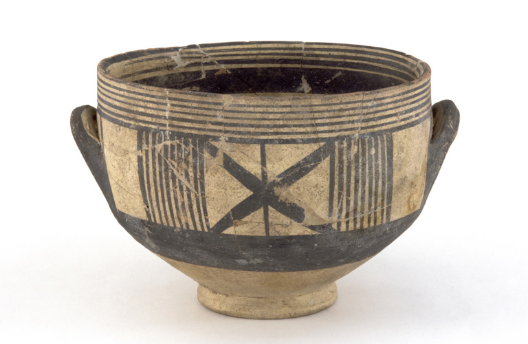 A brown coloured bowl with small handles. It has black line markings of different sizes and going in different directions. There are a few cracks and chips around the top edge of the bowl some of which have noticeable repairs to them.   