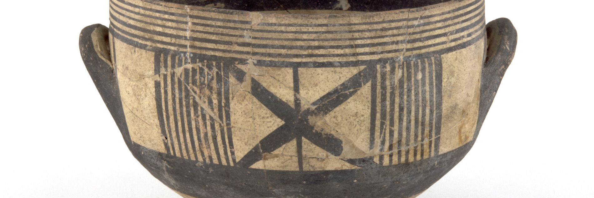 A brown coloured bowl with small handles. It has black line markings of different sizes and going in different directions. There are a few cracks and chips around the top edge of the bowl some of which have noticeable repairs to them.   