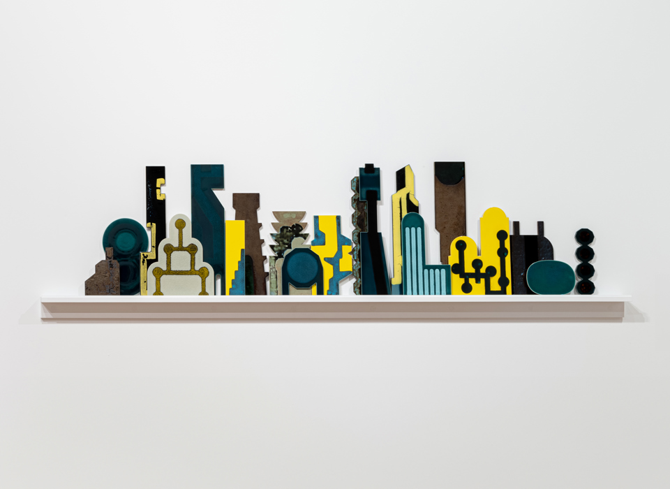 An image of ceramic works placed on a white shelf against a white wall. The ceramics are of various shapes, in blue, yellow, cream and black colours.