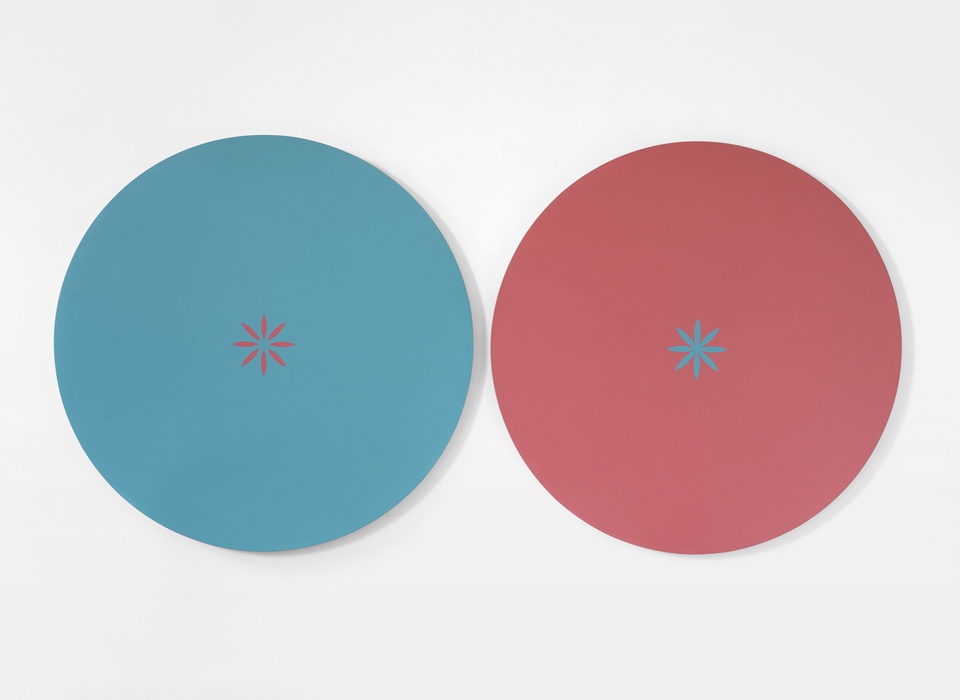 A painting of two coloured circles side by side on a white background. The left circle is blue, with a small pink star at its centre.  The right circle is pink, with a small blue star at its centre. 