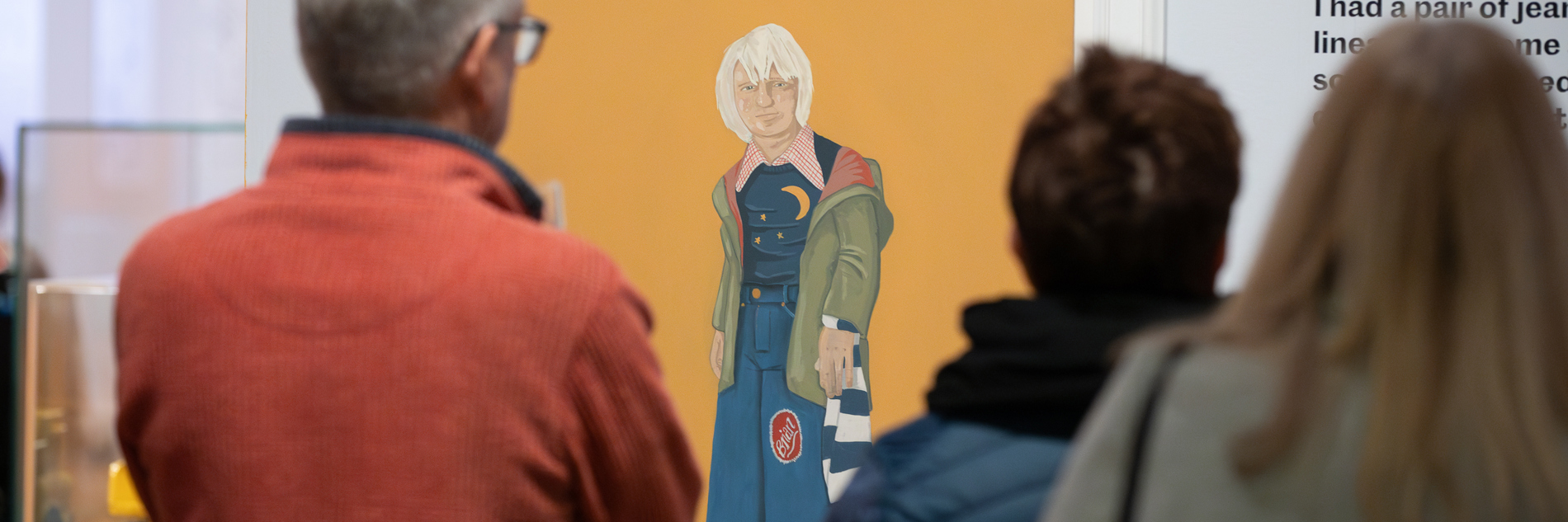 Two people look at a painting of a boy dressed in 1970s clothes 