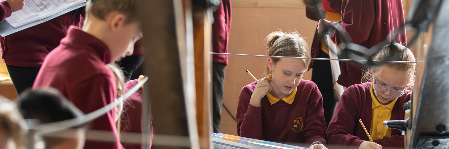 A group of school children writing on clipboards among historic industrial machinery.