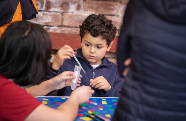 A photograph of a child holding a pipette with an adult holding a test tube in front of them. 