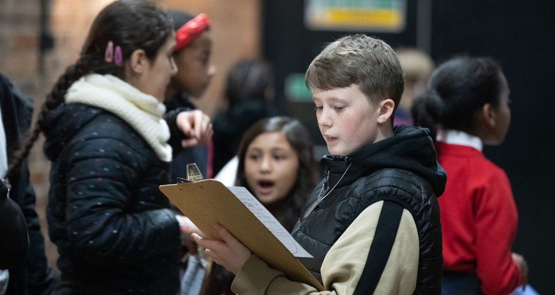 A group of primary school aged children, the child in focus is looking at a clipboard.