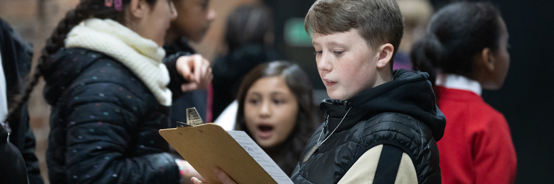 A group of primary school aged children, the child in focus is looking at a clipboard.