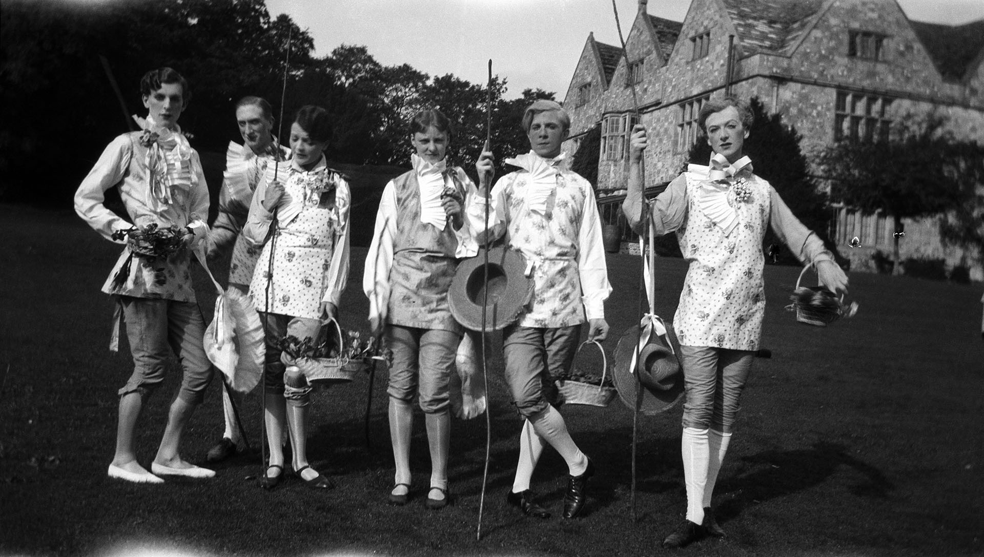 A black and white photograph of a group of adults in the gardens of a large house.  