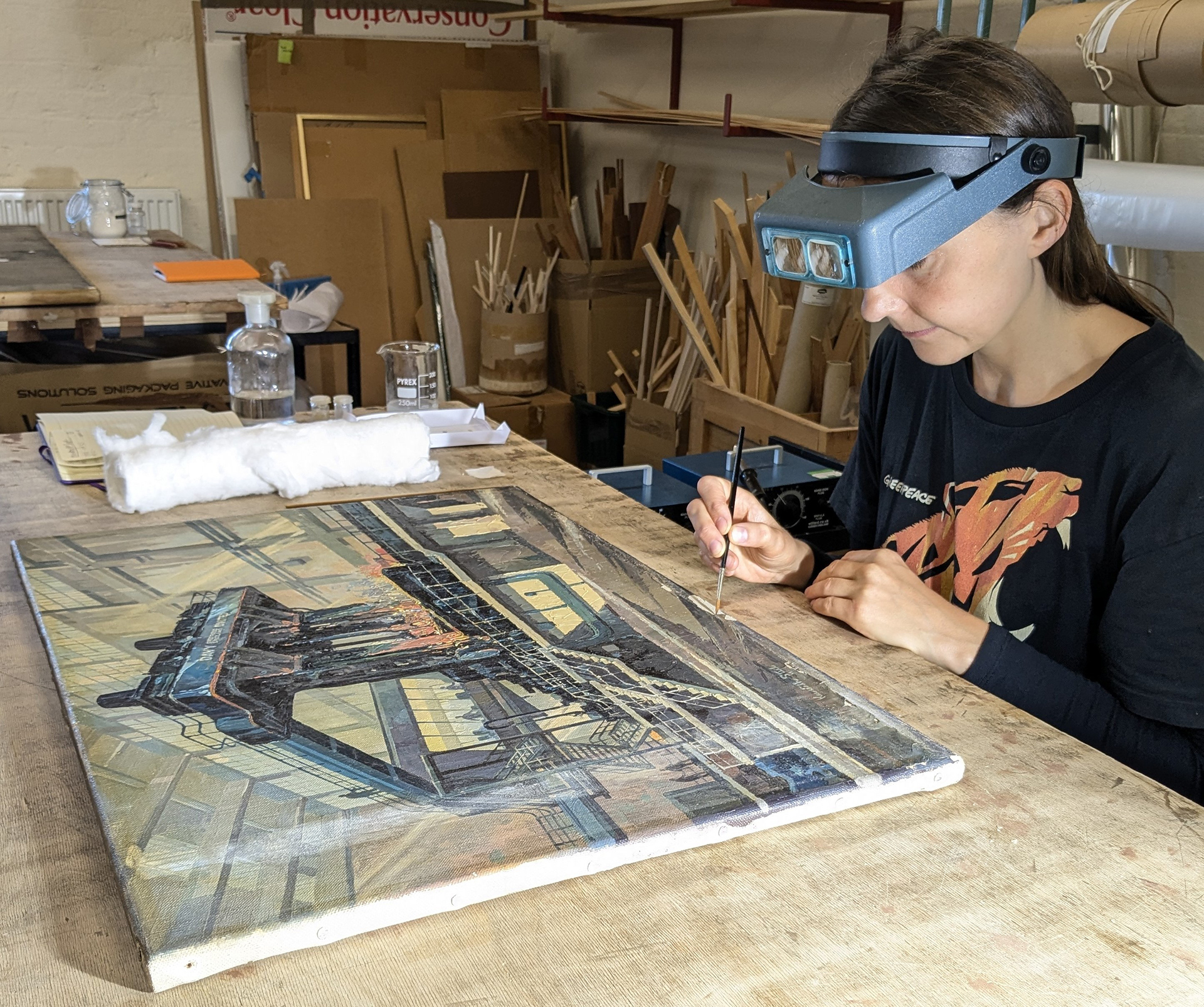 Conservator Lucy Critchlow wears magnifying glasses as she uses a fine paint brush to consolidate the paint layer.