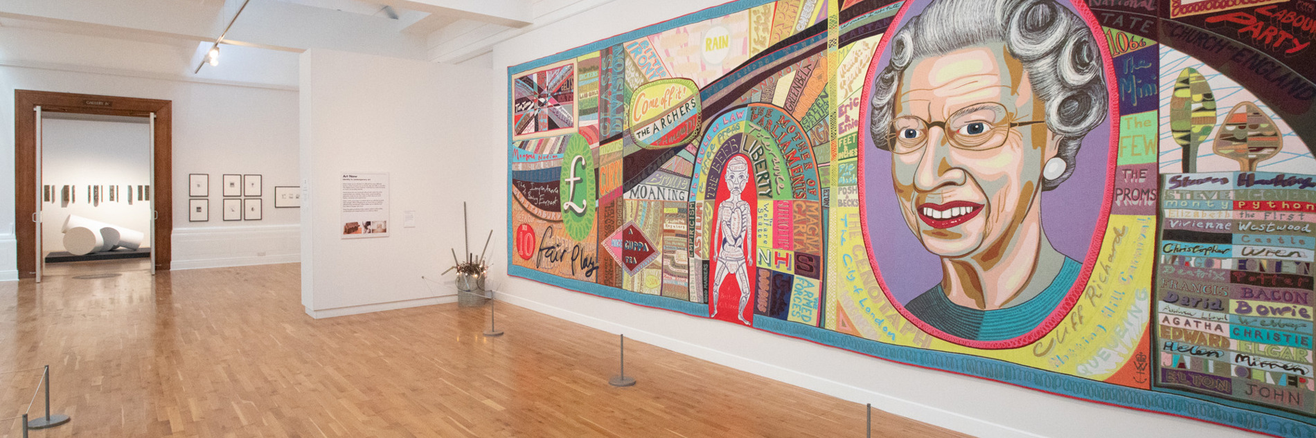 A photograph showing Grayson Perry's Comfort Blanket in Graves Gallery. It is a large patchwork quilt, with a large portrait of Queen Elizabeth 2nd on it.