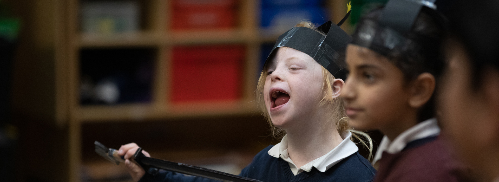 Two children wearing paper helmets and holding clipboards.