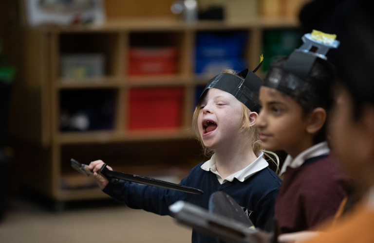 Two children wearing paper helmets and holding clipboards.