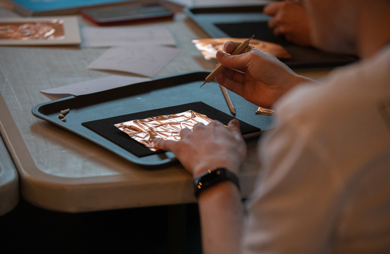 A close up of someone embossing shapes into a thin copper sheet. 