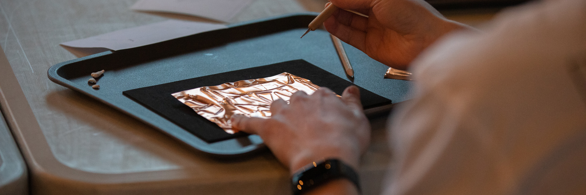 A close up of someone embossing shapes into a thin copper sheet. 