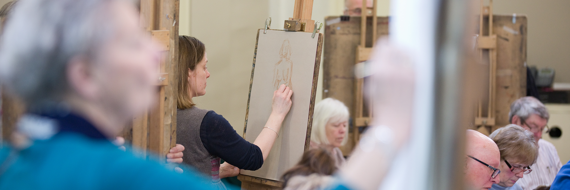 A group of artists standing at easels and sitting at desks drawing. 