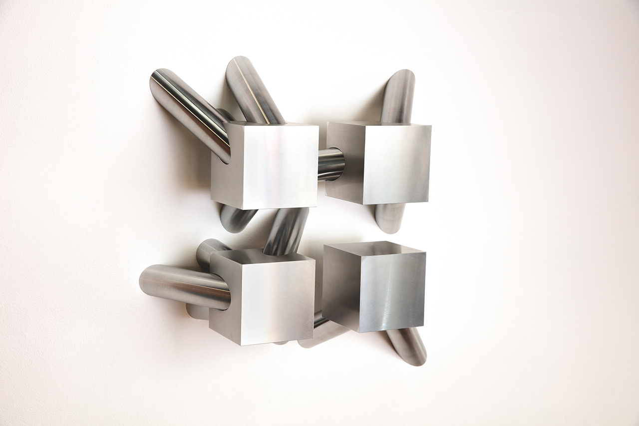 A aluminium metal sculpture of four cubes, arranging in a square shape, with several cylindrical shapes extending from them.