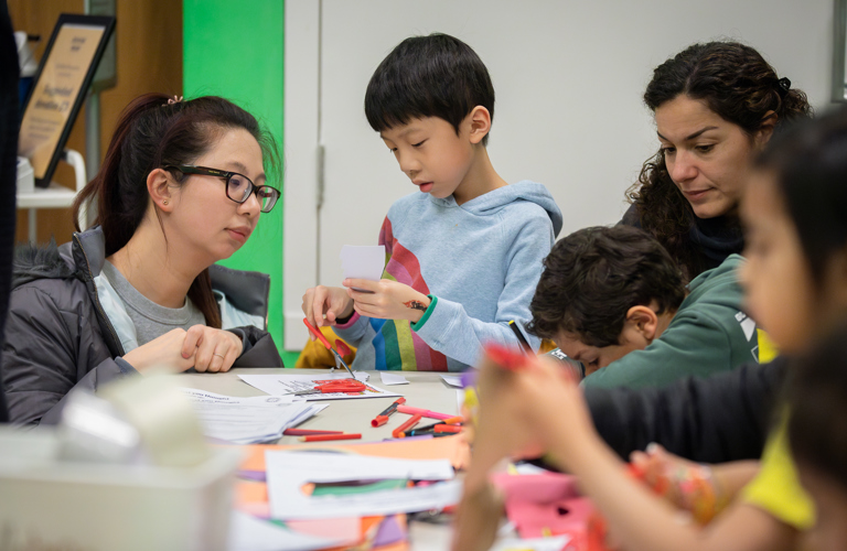A mother-figure and child concentrating on cutting and sticking.