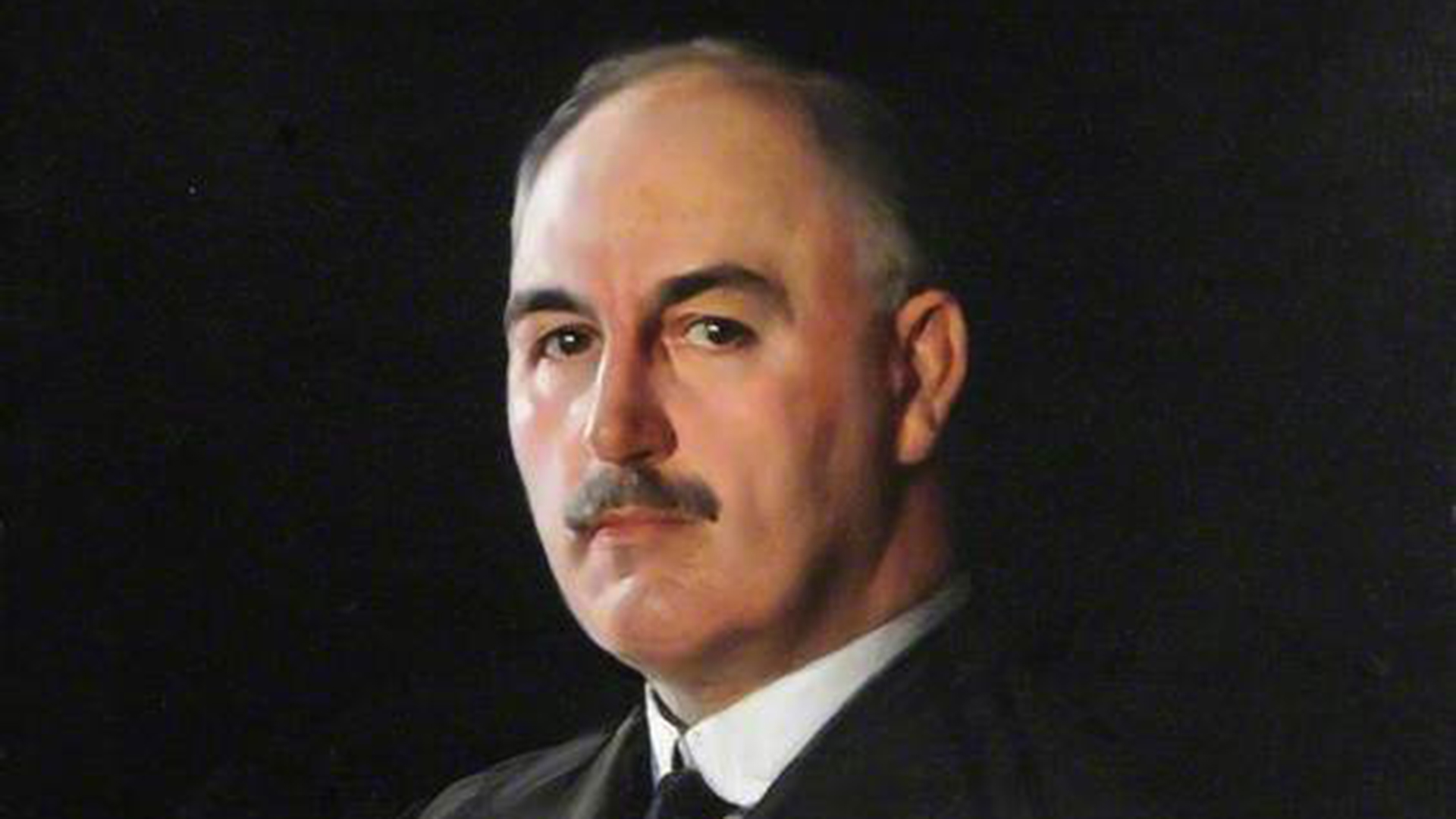 A portrait painting of Dr J.G Graves at around 77 years old. He looks out from the canvas directly with a serious expression and has short, grey hair, a neat moustache and he's wearing a dark suit againist a plain, black background. 