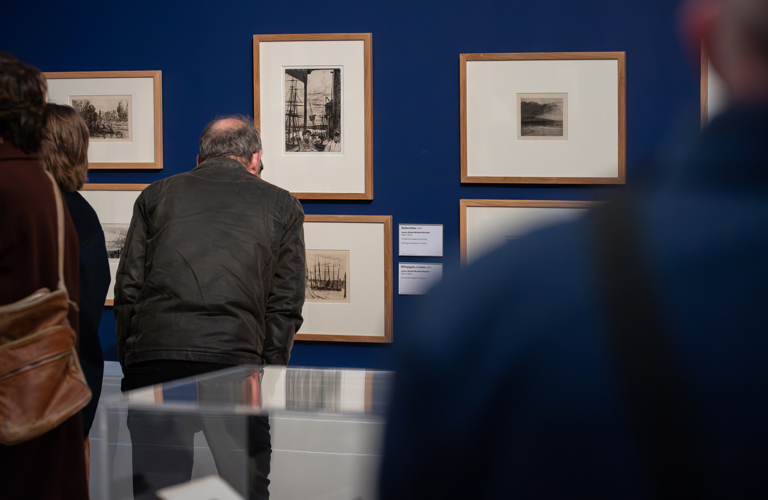 A photograph of adults looking at artworks in a gallery. 