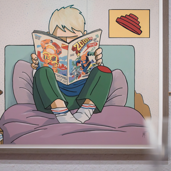 A colourful painting of a child on a bed reading a 2000AD comic