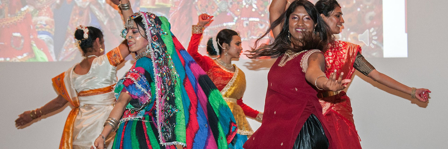 A group of adults dancing in a circle in South Asian traditional dress. 