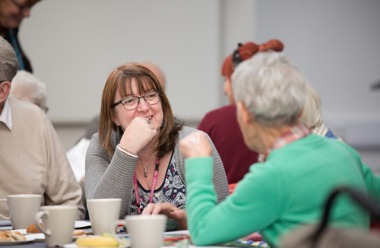 A group of adults talking, the one facing the camera is smiling. 