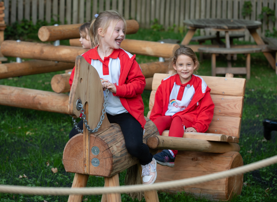 Two children play on a wooden horse and cart in a outdoor play area