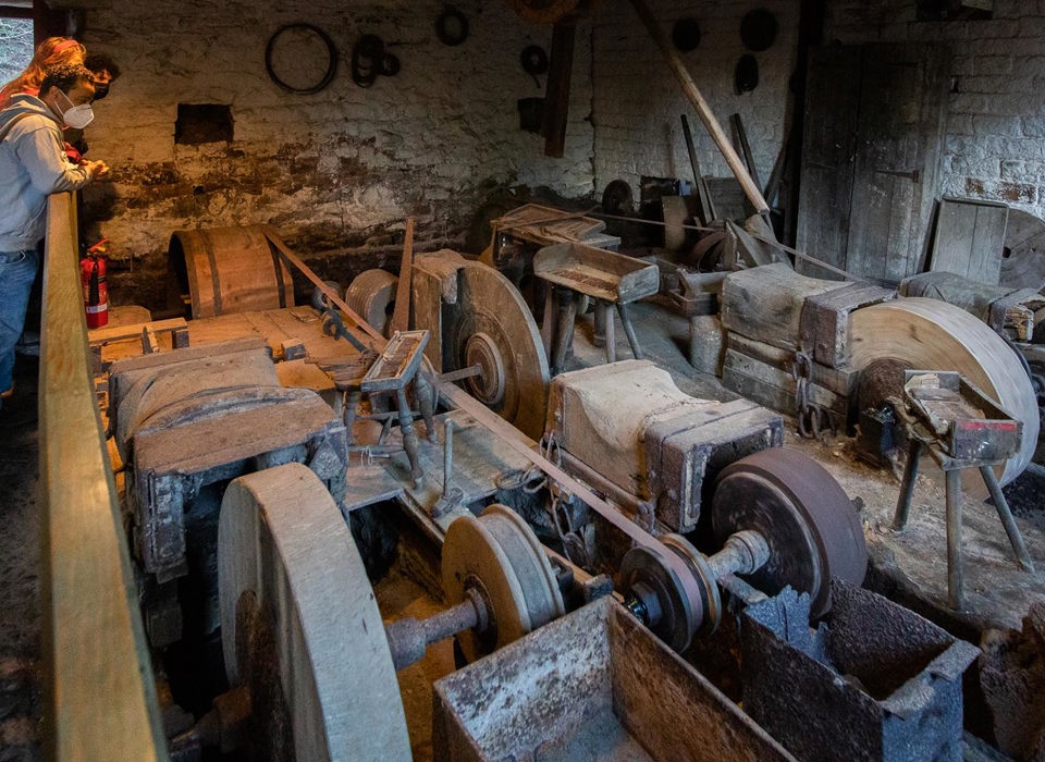 An old workshop with three grindstones. Leaning against the walls are piles of wood, tools and stones of different shapes and sizes.