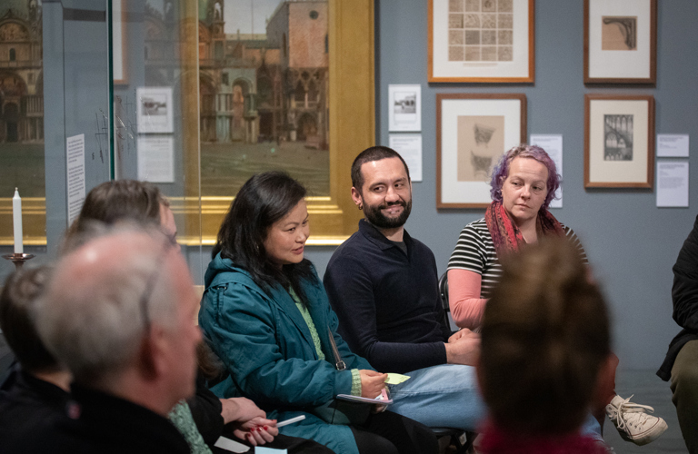 A photograph showing a group of adults sat in chairs in Graves Gallery, talking together. 