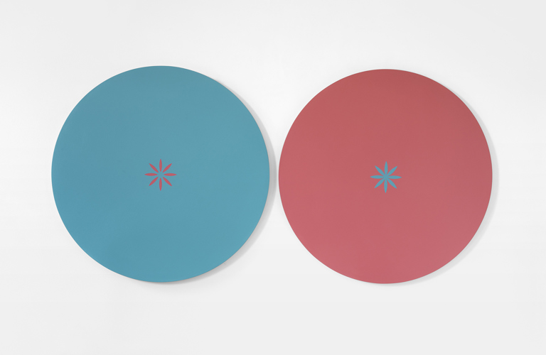 A painting of two coloured circles side by side on a white background. The left circle is blue, with a small pink star at its centre.  The right circle is pink, with a small blue star at its centre. 