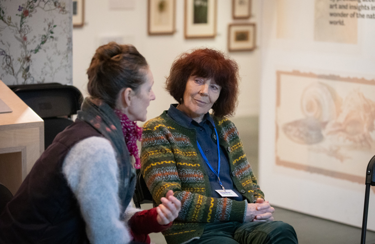 A photograph of two people sat down in conversation in the Ruskin Gallery at Millennium Gallery.