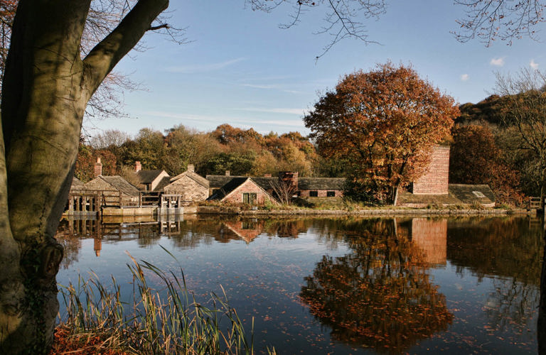 Looking across open water towards Hamlet buildings framed by trees in autumnal shades.