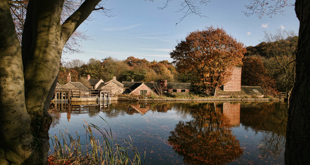 Looking across open water towards Hamlet buildings framed by trees in autumnal shades.