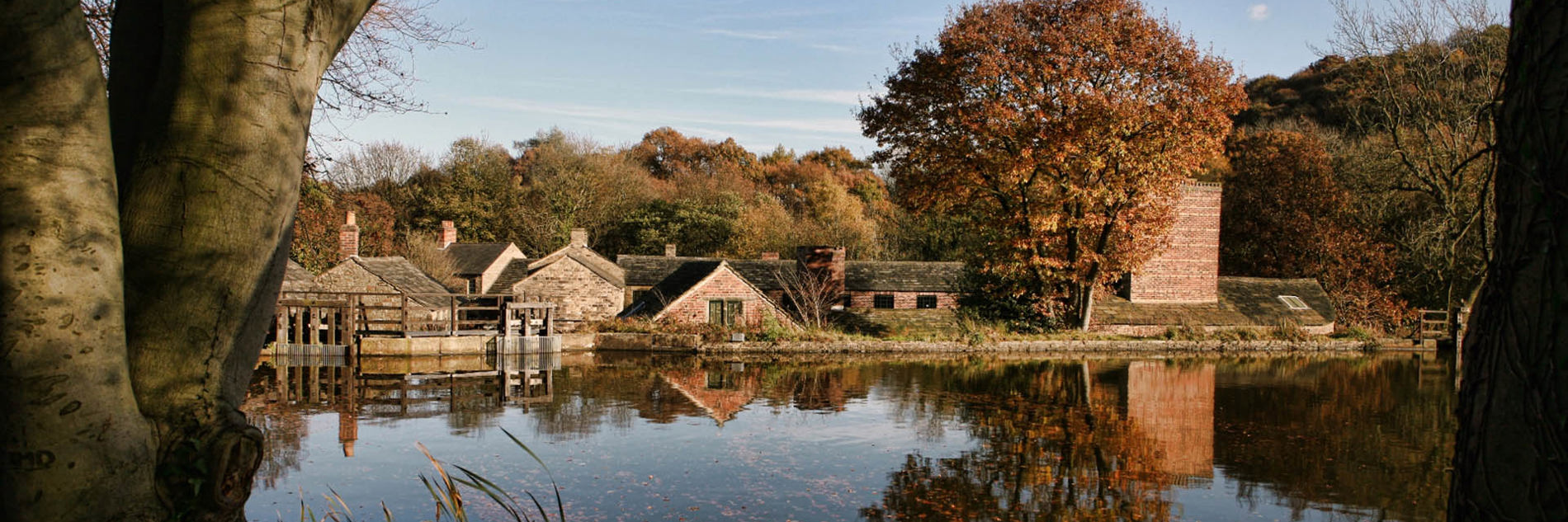 Looking across open water towards Hamlet buildings framed by trees in autumnal shades.