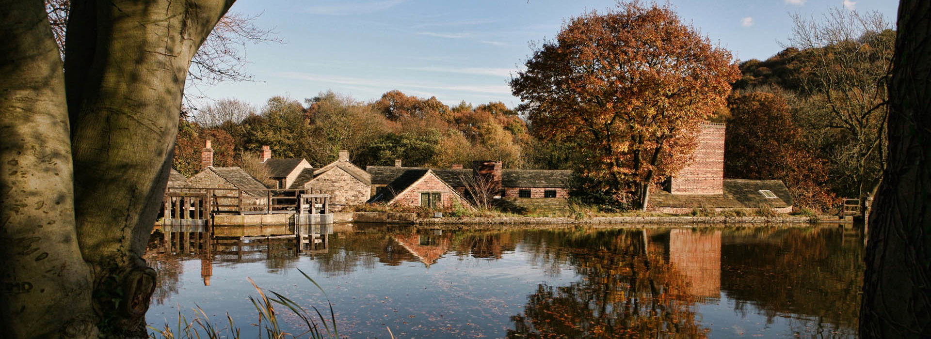 Looking across open water towards Hamlet buildings framed by trees in autumnal shades.