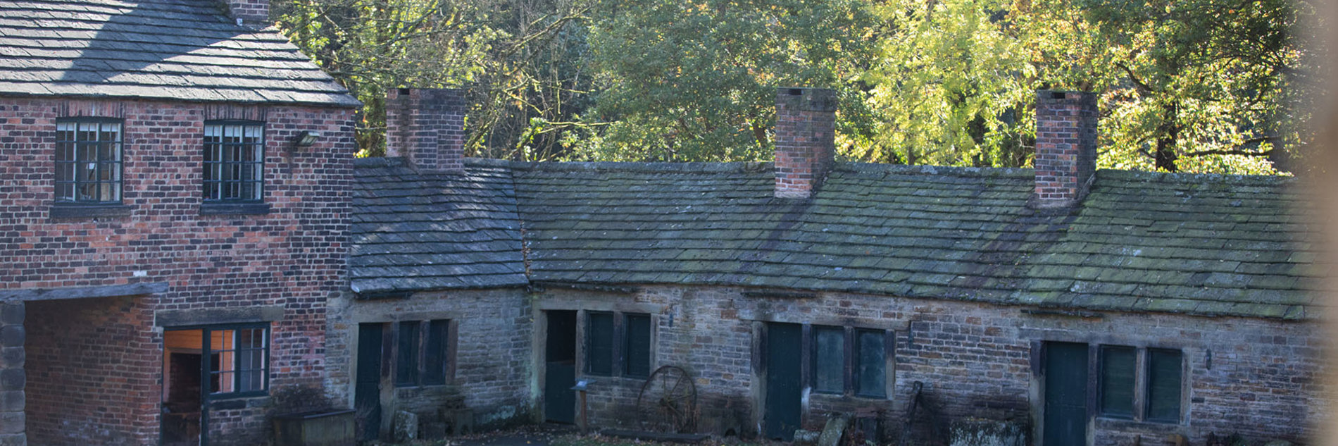 Old stone roofed workshops in a sunny woodland setting.