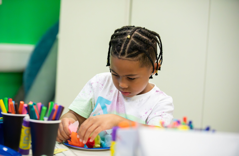 A child creating an artwork using coloured pens and sticking materials.