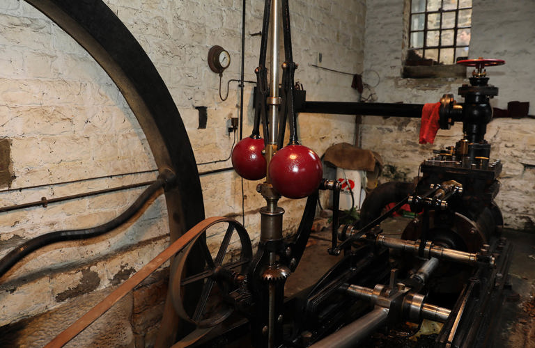 Partial detail of steam engine mechanisms with a focus on the centrifugal governor and belt driven pulley.