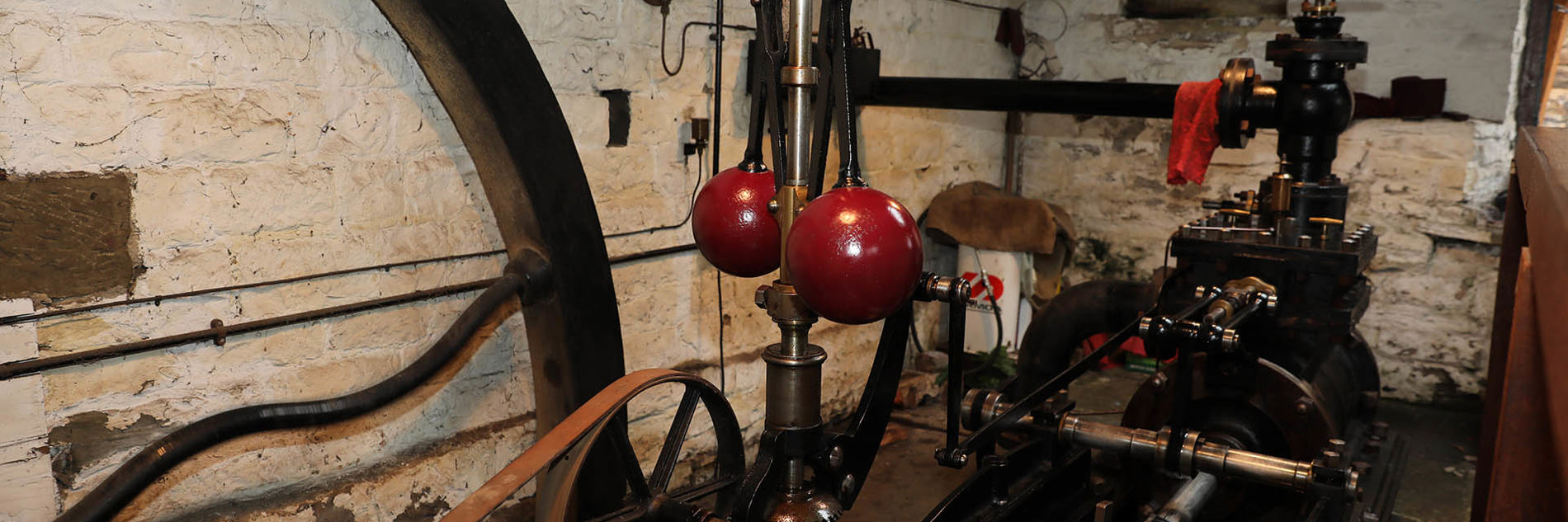 Partial detail of steam engine mechanisms with a focus on the centrifugal governor and belt driven pulley.