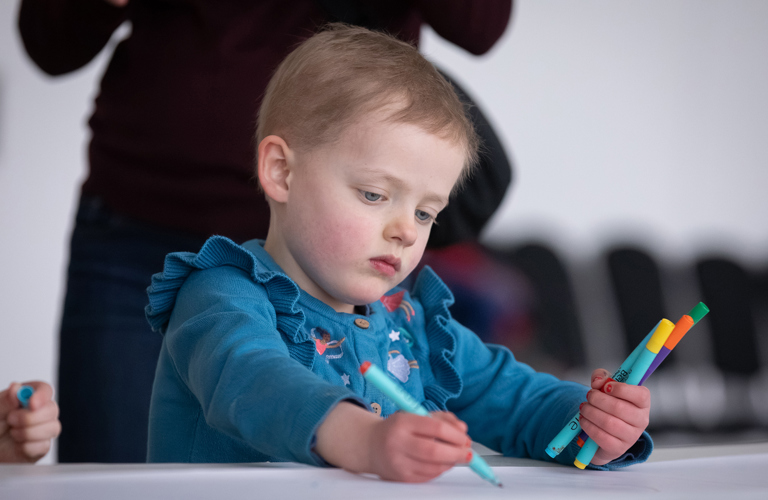 A child in a blue top drawing with coloured pens.