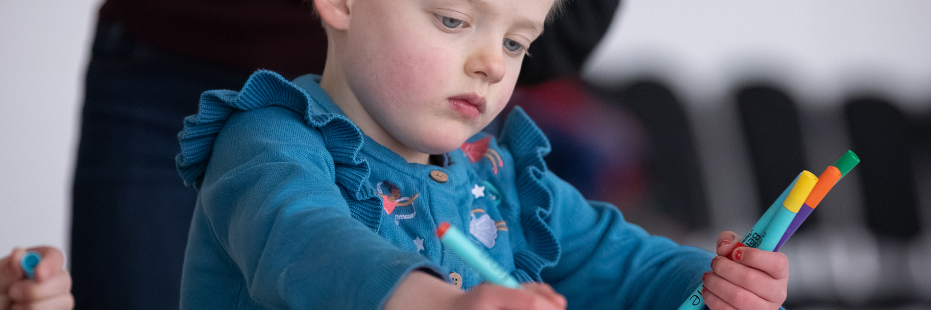A child in a blue top drawing with coloured pens.