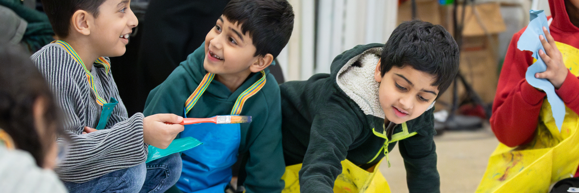 Children smile and chat as they kneel on teh floor and contribute to a large-scale artwork