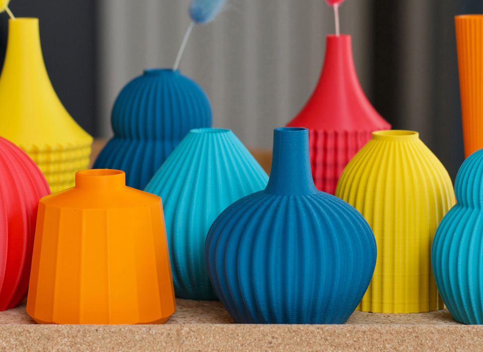 A collection of coloured vases in red, orange, yellow, blue and turquoise. The vases vary in size and shape, but each has a ridged or textured surface.