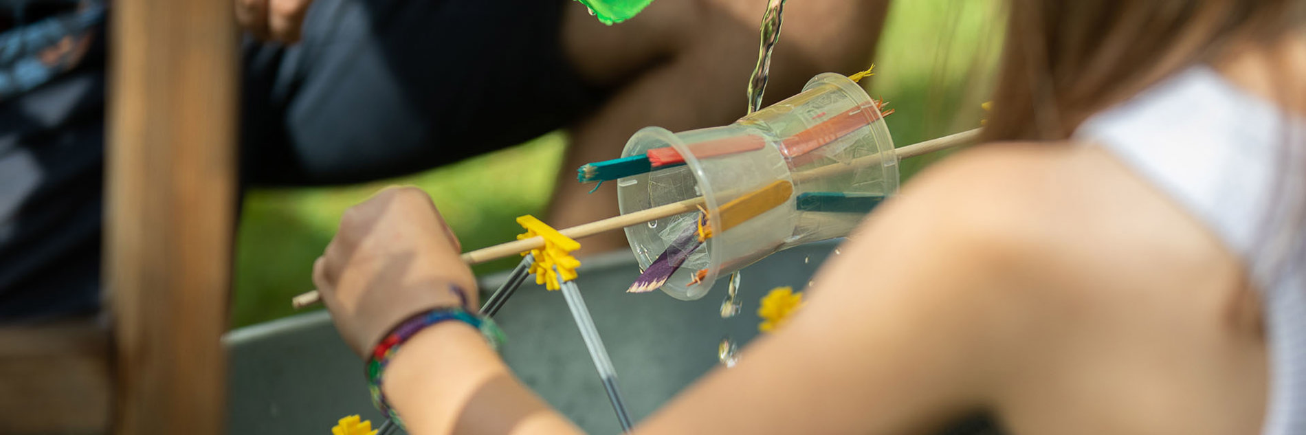 A child testing a crafted waterwheel, made from plastic cups and lollipop sticks.