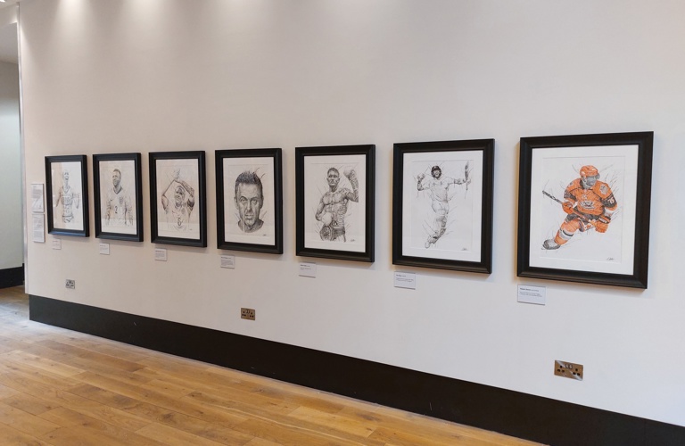 A photograph of 7 drawing of sporting figures on a white wall. 