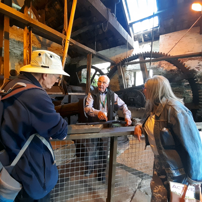 Two adults leaning on a barrier talking to an adult standing in front of historic engineering equipment 