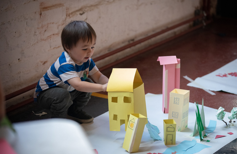 A photograph of a child making buildings from coloured paper. 