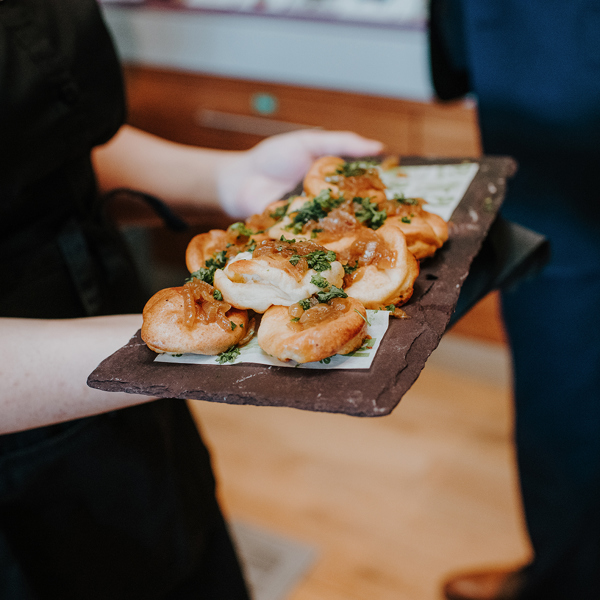 A person's hands holding a slate full of appetisers. 