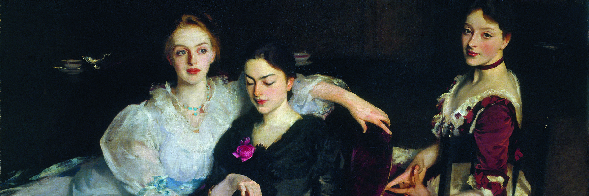 An oil painting of three women in formal Victorian dress. They are sitting informally next to each other - two women are sharing a chair and looking at a book, and the third woman is sitting on a chair behind them. The painting has a dark background, with the outline of a dresser on which sits a silver jug and a porcelain bowl. 